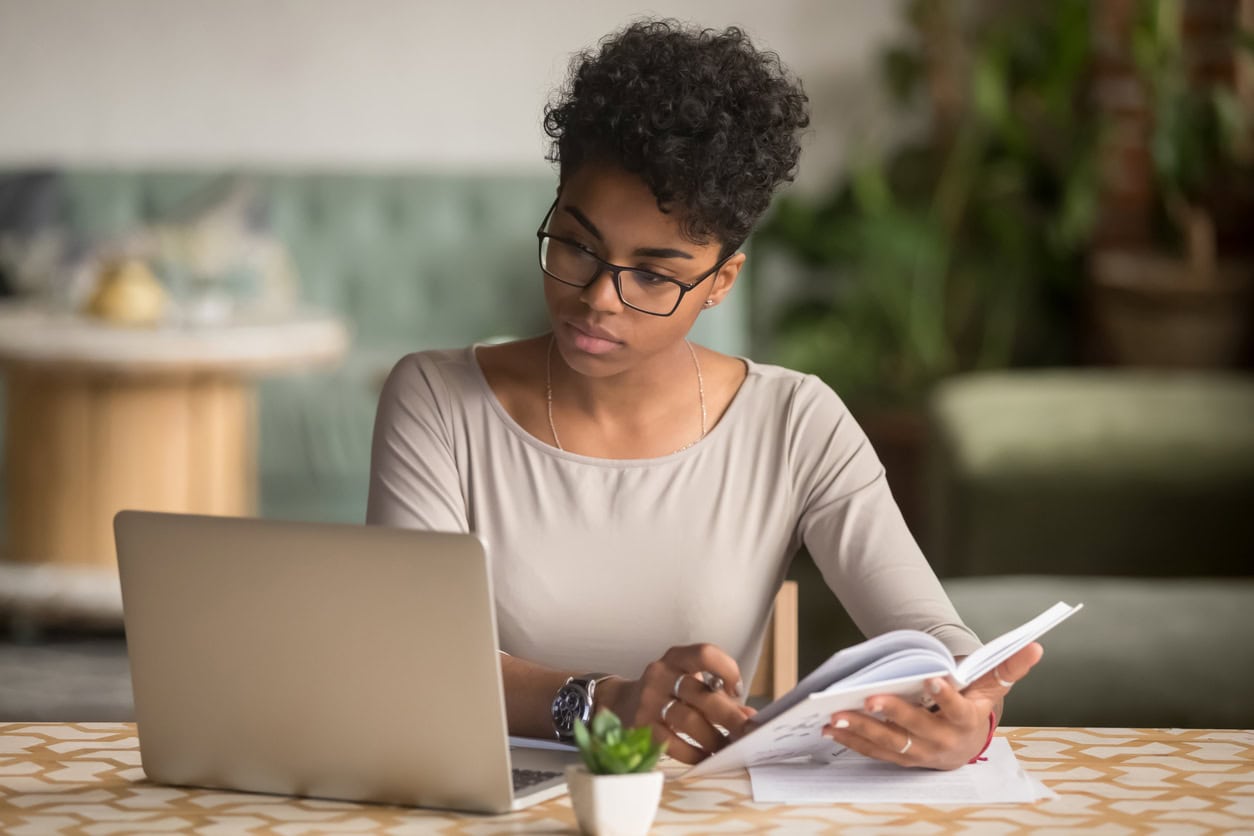 Focused student looking at laptop holding book doing research