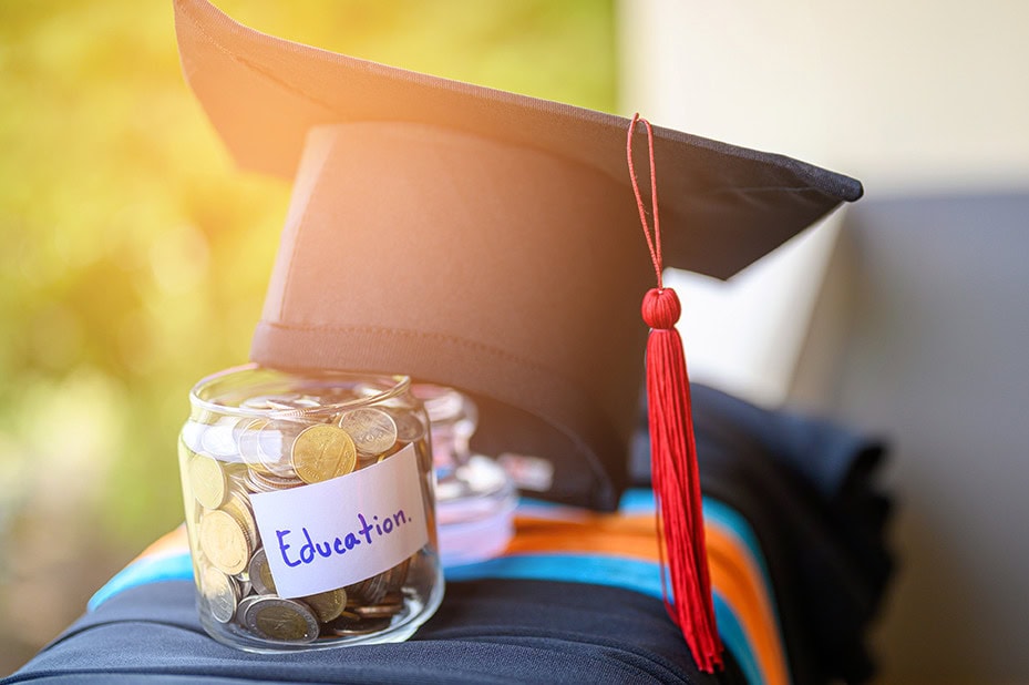 Grad cap and money jar with "Education" label for concept of paying for college