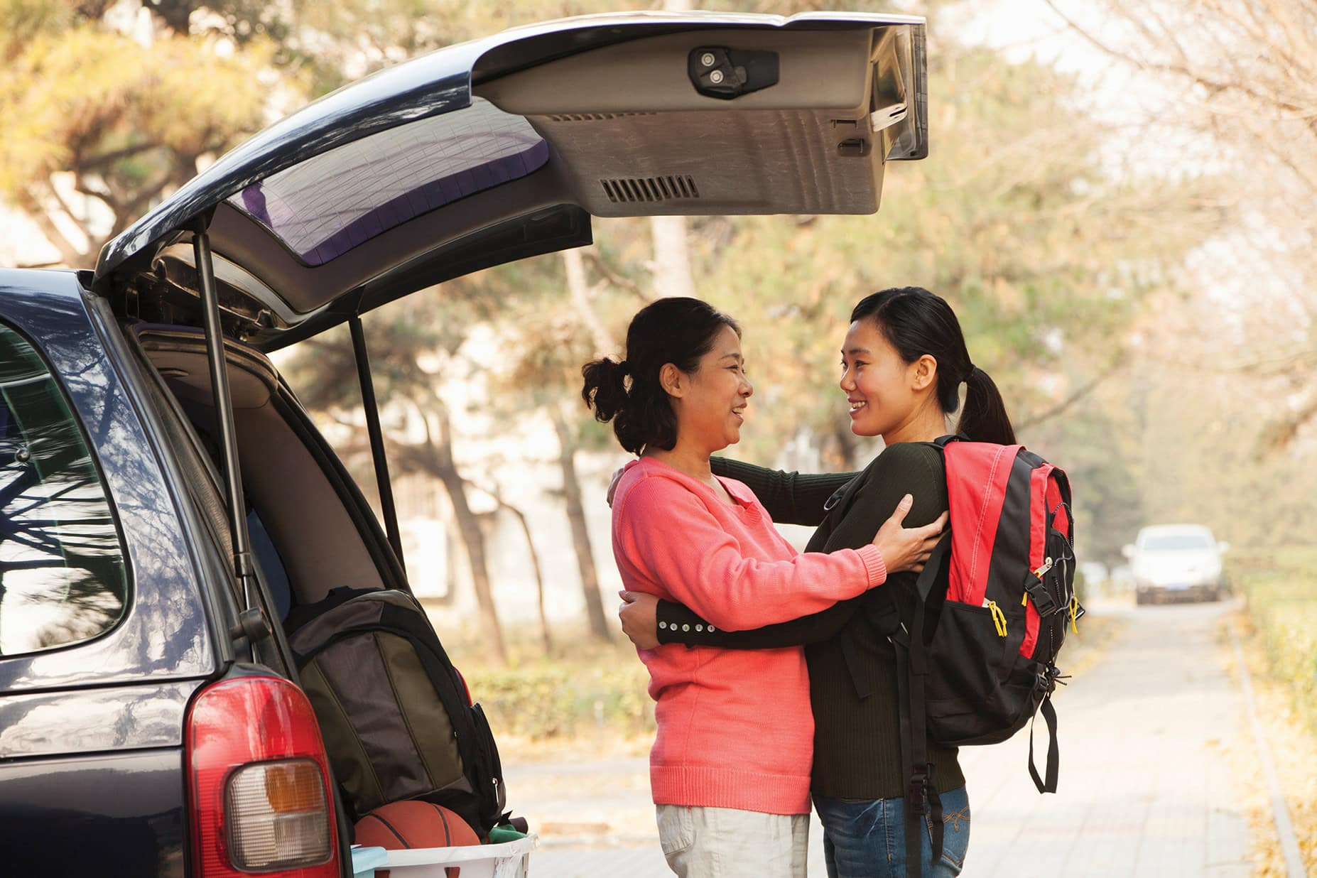 Mom and daughter embracing by car
