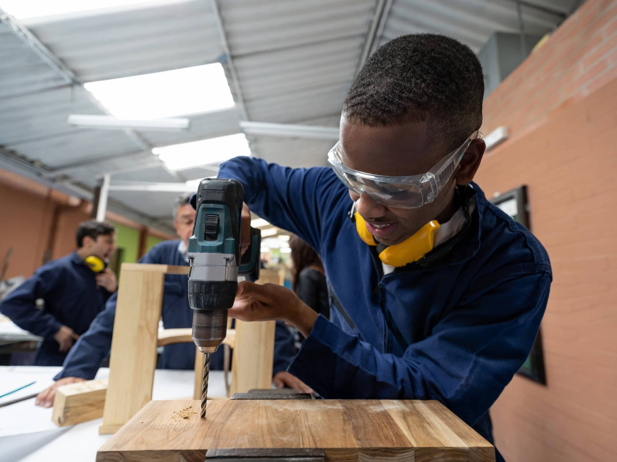 Design student making a piece of furniture in class and drilling a piece of wood - education concepts