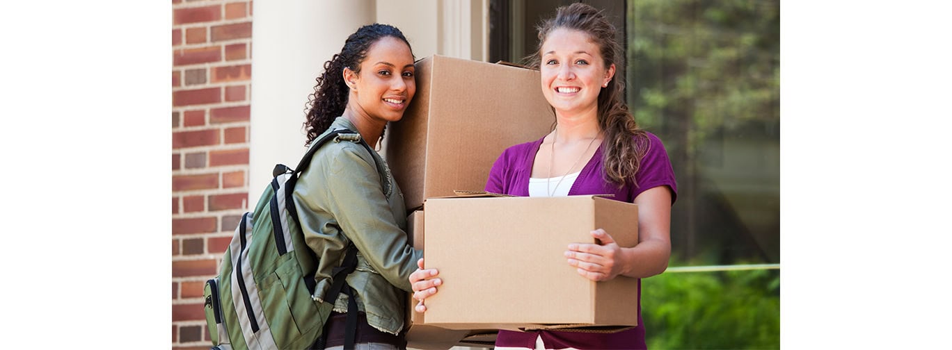 Young women holding boxes moving into college dorm