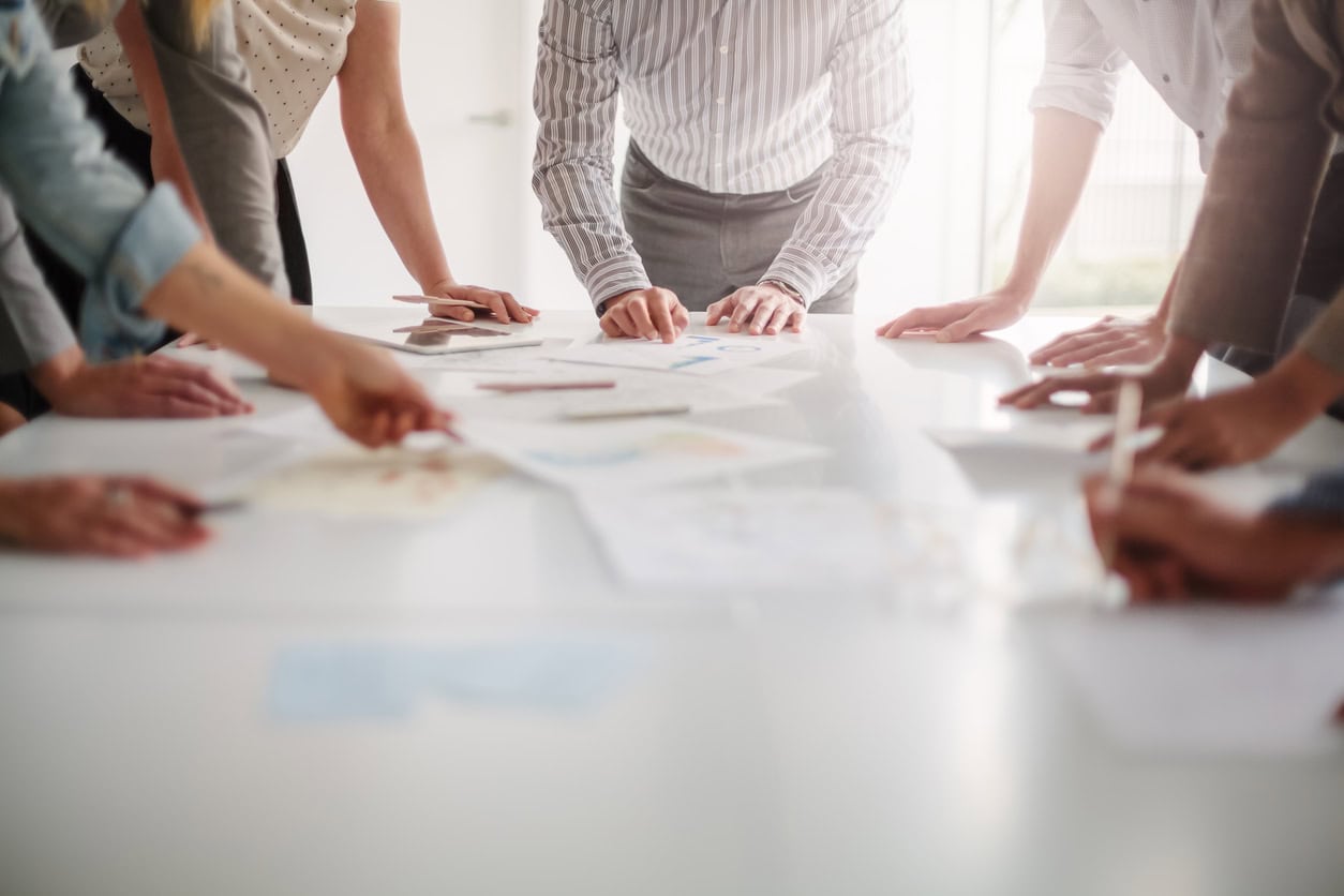 Low angle view of hands of multiracial group of people working with ideas and brainstorming together to make decisions with documents on table Low angle view of hands of multiracial group of people working with ideas and brainstorming together to make decisions with documents on table