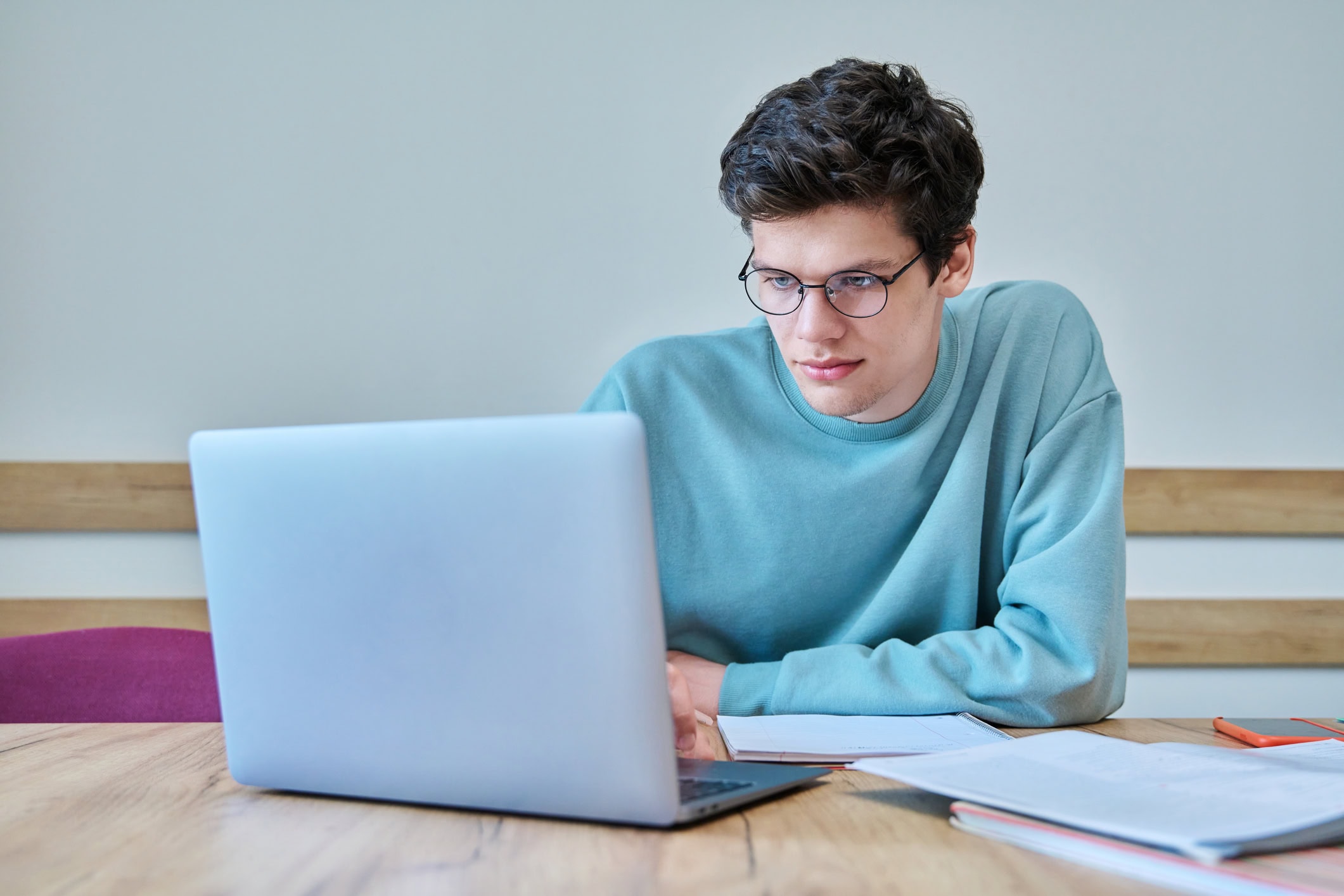 Young guy college student sitting at desk in classroom, using laptop, writing in notebook