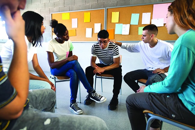 Sad hispanic male high school student sharing bad news with classmates. Multiracial teenagers sitting in circle