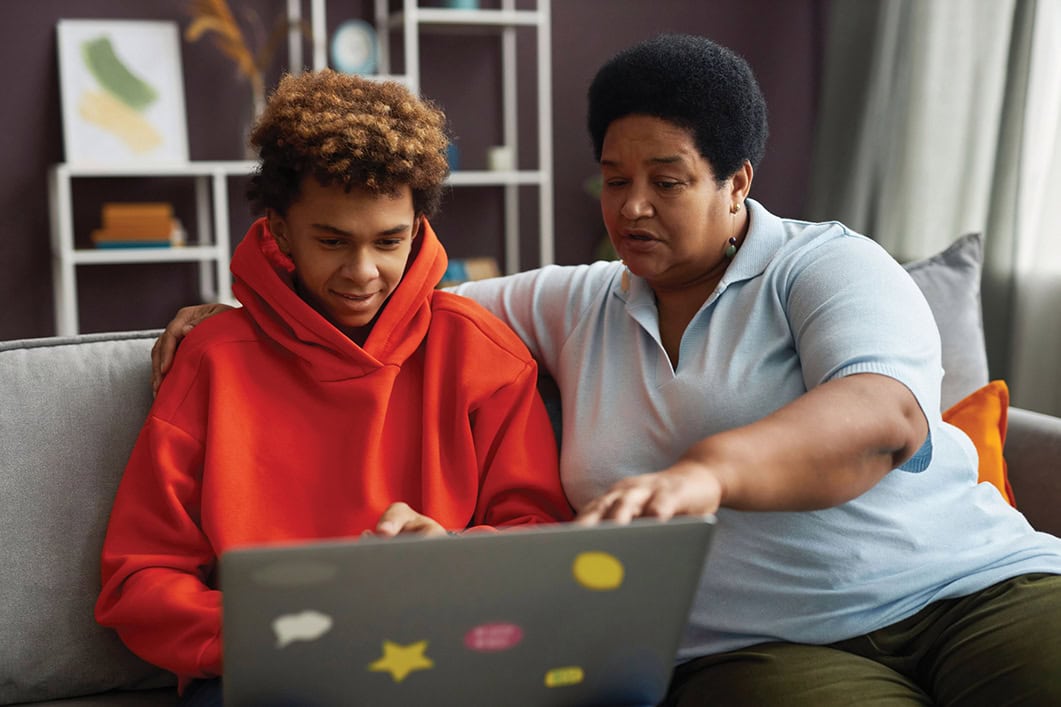 African American mature woman and teenage boy looking at laptop screen