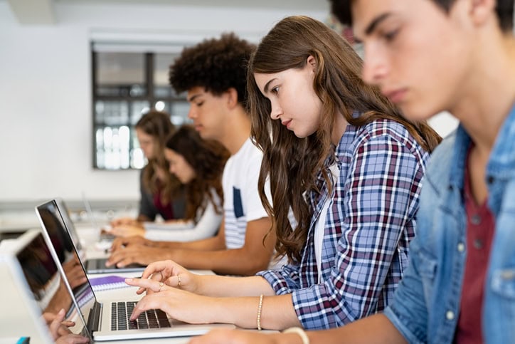 Multiethnic college students sitting in a classroom studying on laptop during class. Group of guys and girls using laptop during computer lesson. Young man and concentrated women sitting in a row and working on computers.