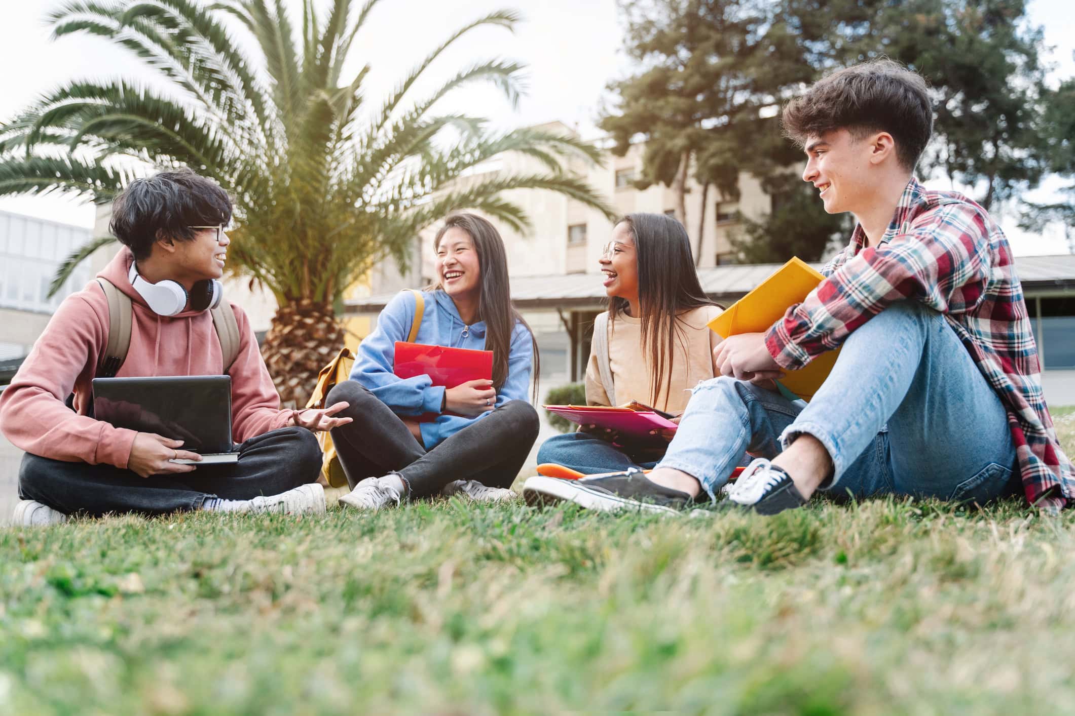 Group of multiracial international exchange student friends sitting on the grass on school campus