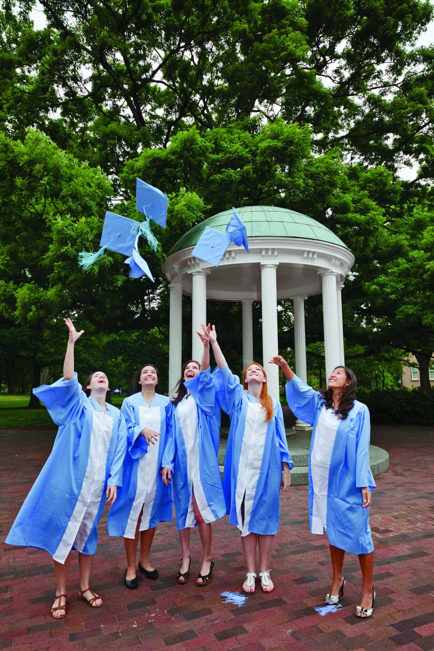 Chapel Hill, North Carolina, USA - April 28, 2012: Five female senior undergraduate students who are about to graduate with a bachelors degree are wearing their light blue colored cap and gown and are practicing the cap toss in front of the Old Well