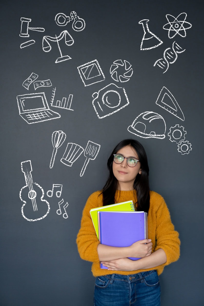 Happy student thinking about what to study as her major and looking at the options on a blackboard