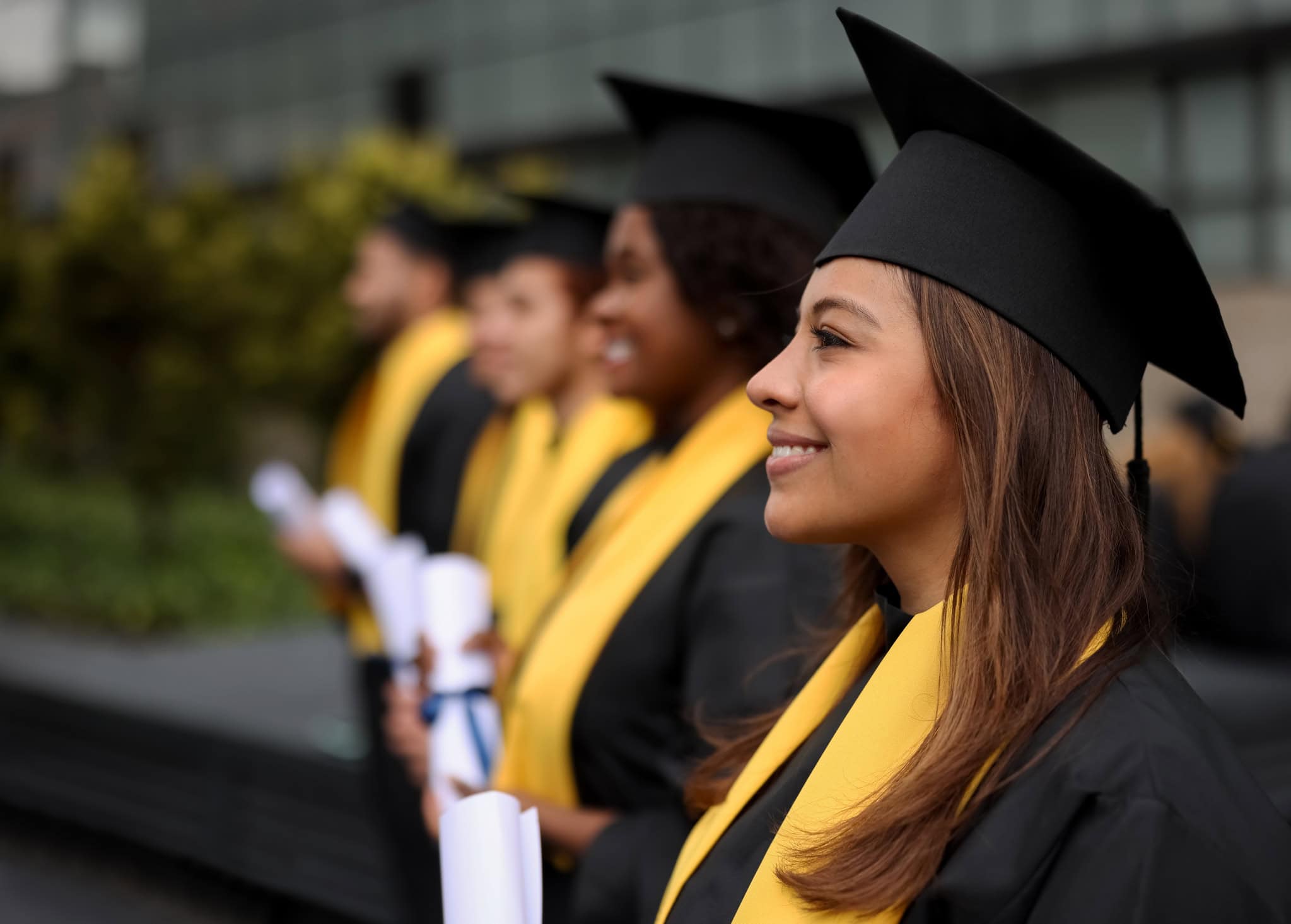 Happy group of graduate students in a row holding their diplomas on their graduation day and smiling