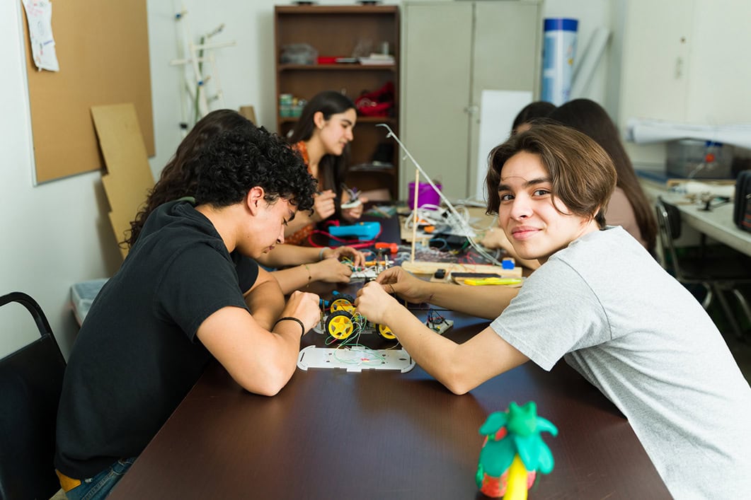 Group of high school students building a robot for their stem project using electronic components during science class