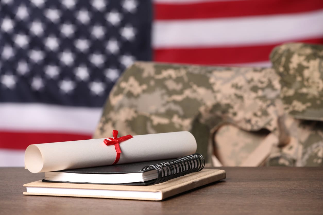 Notebooks and diploma on wooden table, chair with soldier uniform against flag of United States indoors.