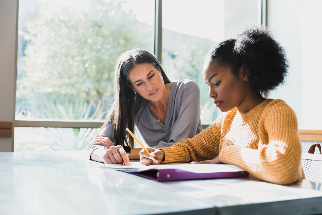 A mid adult female teacher spends one-on-one time helping the teenage girl with her homework.