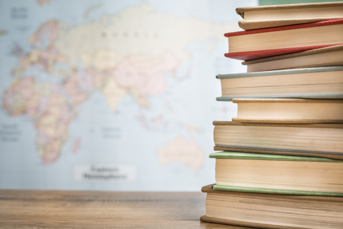 Textbooks stacked on wooden school desk in front of world map.